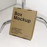Free Cardboard Box Leaning Against the Tripod Mockup